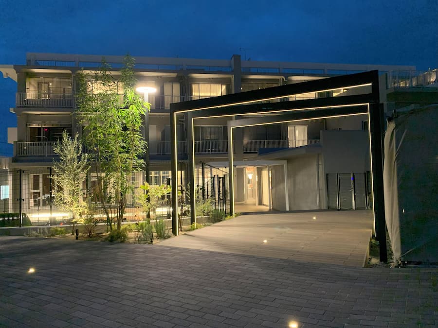 Un edificio moderno con entrada cubierta, varios balcones y un área exterior bien iluminada con suelo empedrado.