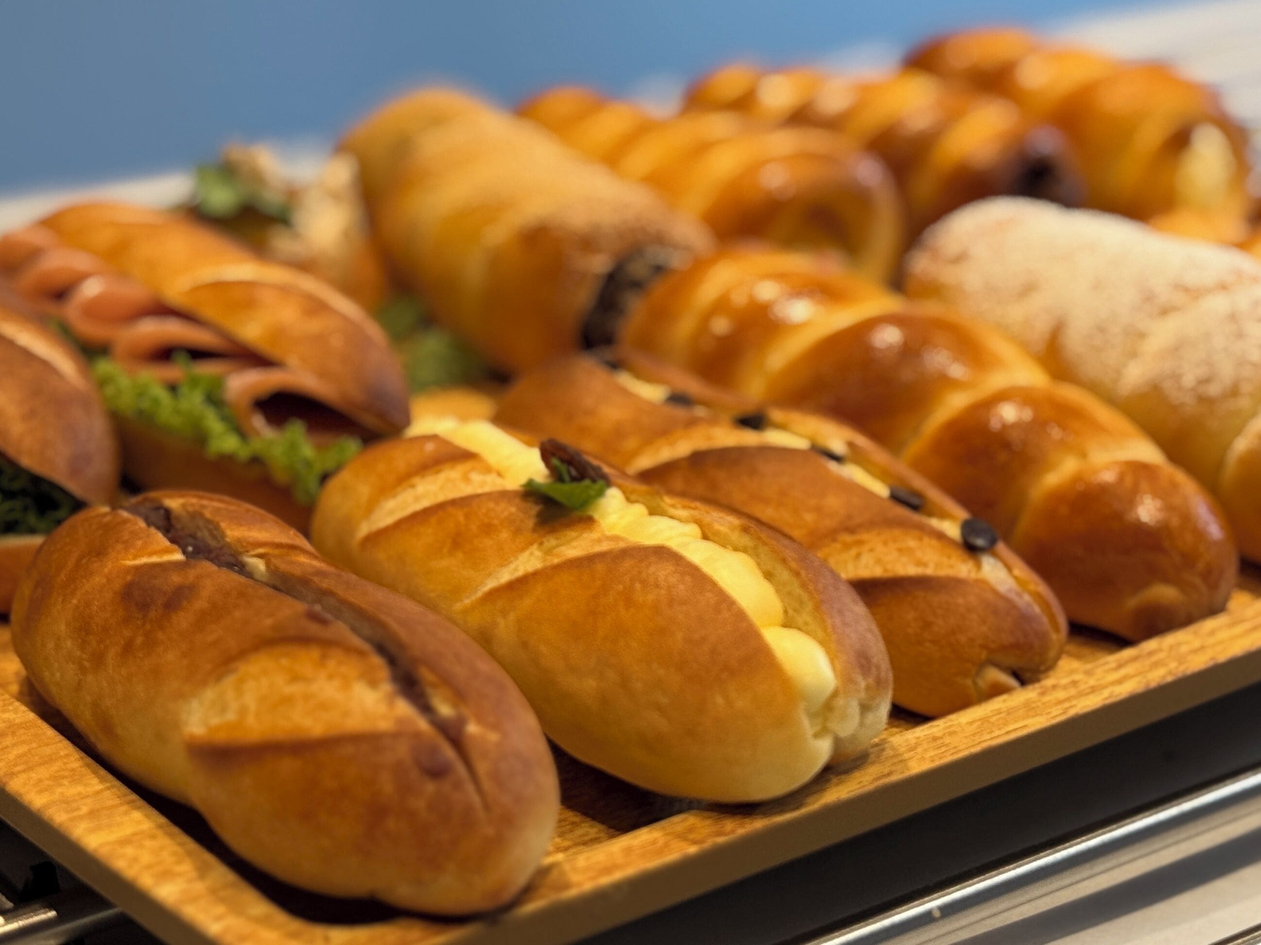 A tray of assorted baked goods, including croissants and rolls, on a wooden surface.