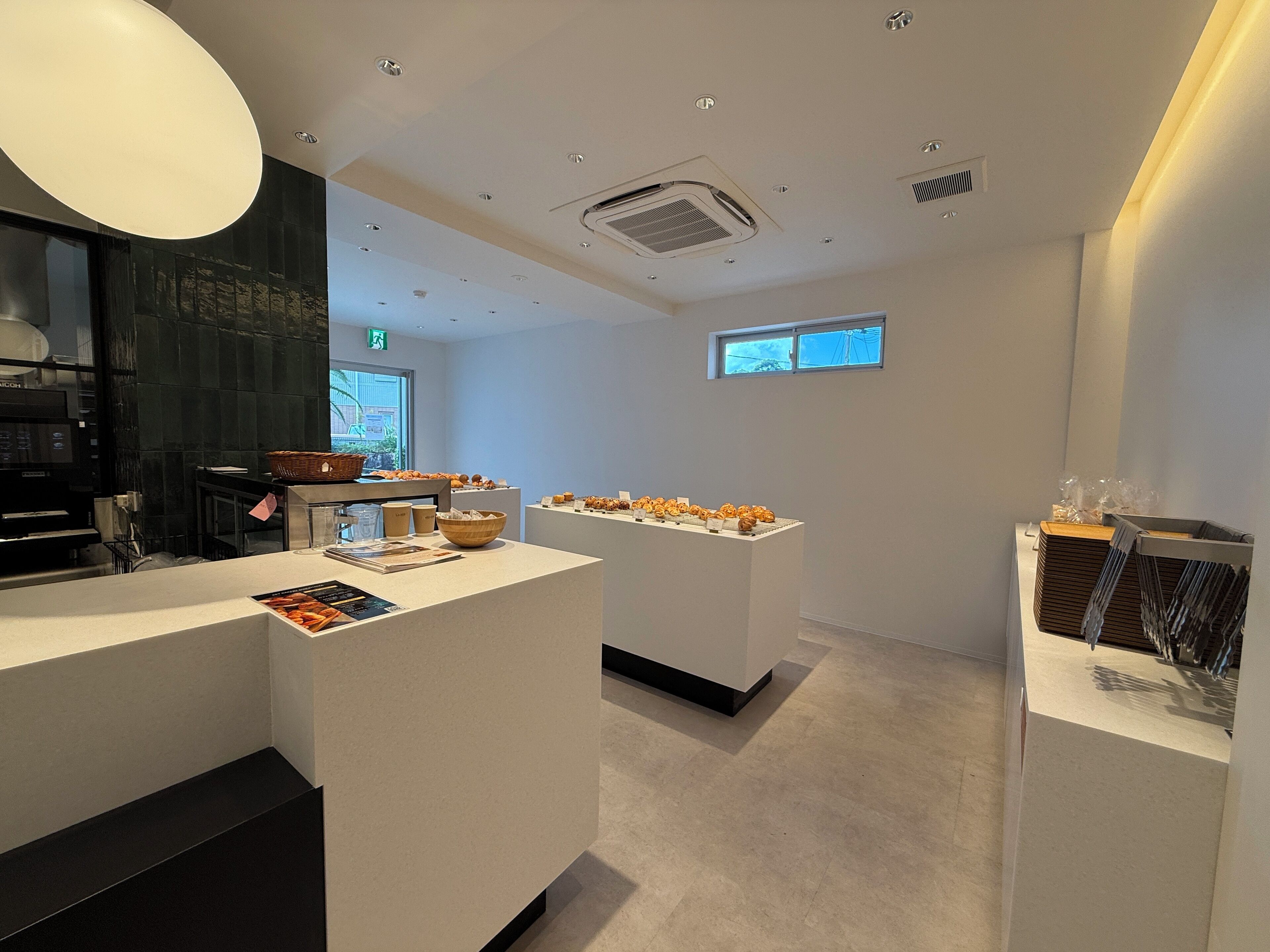 A modern cafe with a clean, minimalist design, featuring a central counter with pastries and a seating area with tables and chairs.
