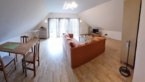 En moderne loftlejlighed med spiseplads, sofa, fjernsyn og et stort vindue.