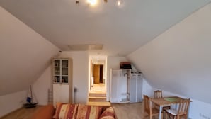En rummelig stue med en stor sofa, et spisebord med stole, og et køkkenområde i baggrunden.