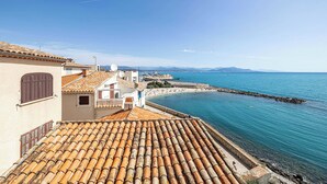 A coastal town with terracotta-tiled rooftops, a clear blue sea, and a rocky breakwater.