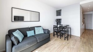 A modern living room with a grey sofa, a dining table with chairs, and a large mirror on the wall.