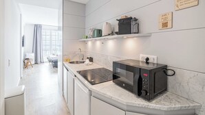 A modern kitchen with a built-in microwave, a kettle, and a coffee maker on the countertop. There are two shelves above the counter, and a sign on the wall.