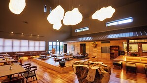 Un restaurant spacieux avec des tables et des chaises en bois, une grande sculpture en bois comme élément central, et des luminaires suspendus.