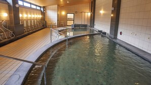 Un espace de bains public comprenant plusieurs vestiaires, une piscine centrale et un espace détente avec des sièges.
