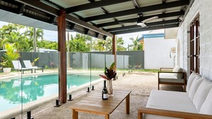 Un espacio al aire libre techado con piscina, sillas de descanso, una mesa y un sofá.