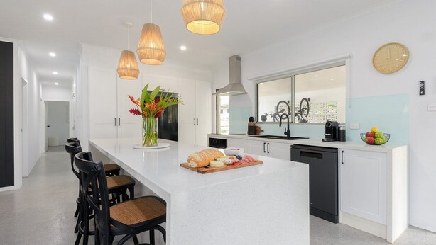 Una cocina moderna con una isla central, taburetes de bar, un florero y un reloj en la pared.