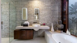 A modern bathroom with a stone wall, a round sink, a large mirror, and a bathtub.