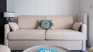 Een beige bank met een decoratief kussen, een lamp en een boek op een tafel.