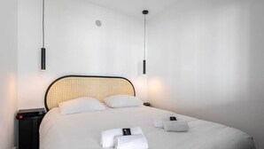 Een opgemaakt bed met witte lakens, een zwart hoofdbord en twee bedlampen.