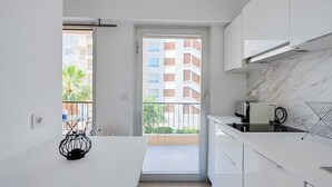 Een moderne keuken met witte kasten, een marmeren aanrechtblad en uitzicht op een balkon met een gebouw op de achtergrond.