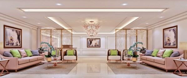 Un salon spacieux, agrémenté d’un lustre central, de deux canapés avec des coussins verts et d’un grand tableau accroché au mur.