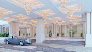 A grand entrance with multiple chandeliers, a Rolls-Royce parked outside, and a marble floor. - OZEN MANSION KOLKATA (Barasat)