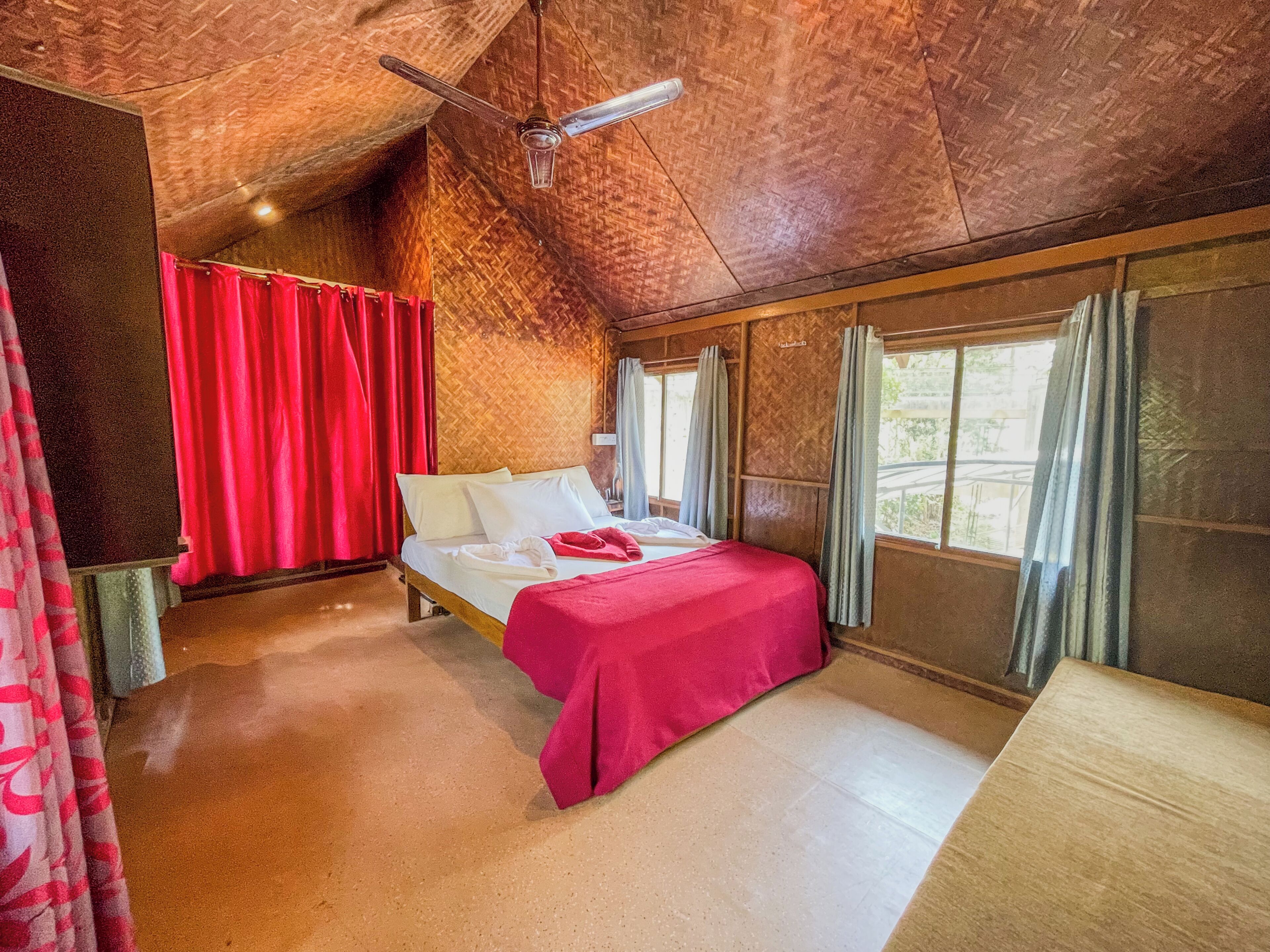 Quarto com cama, ventilador de teto e janela com cortinas.