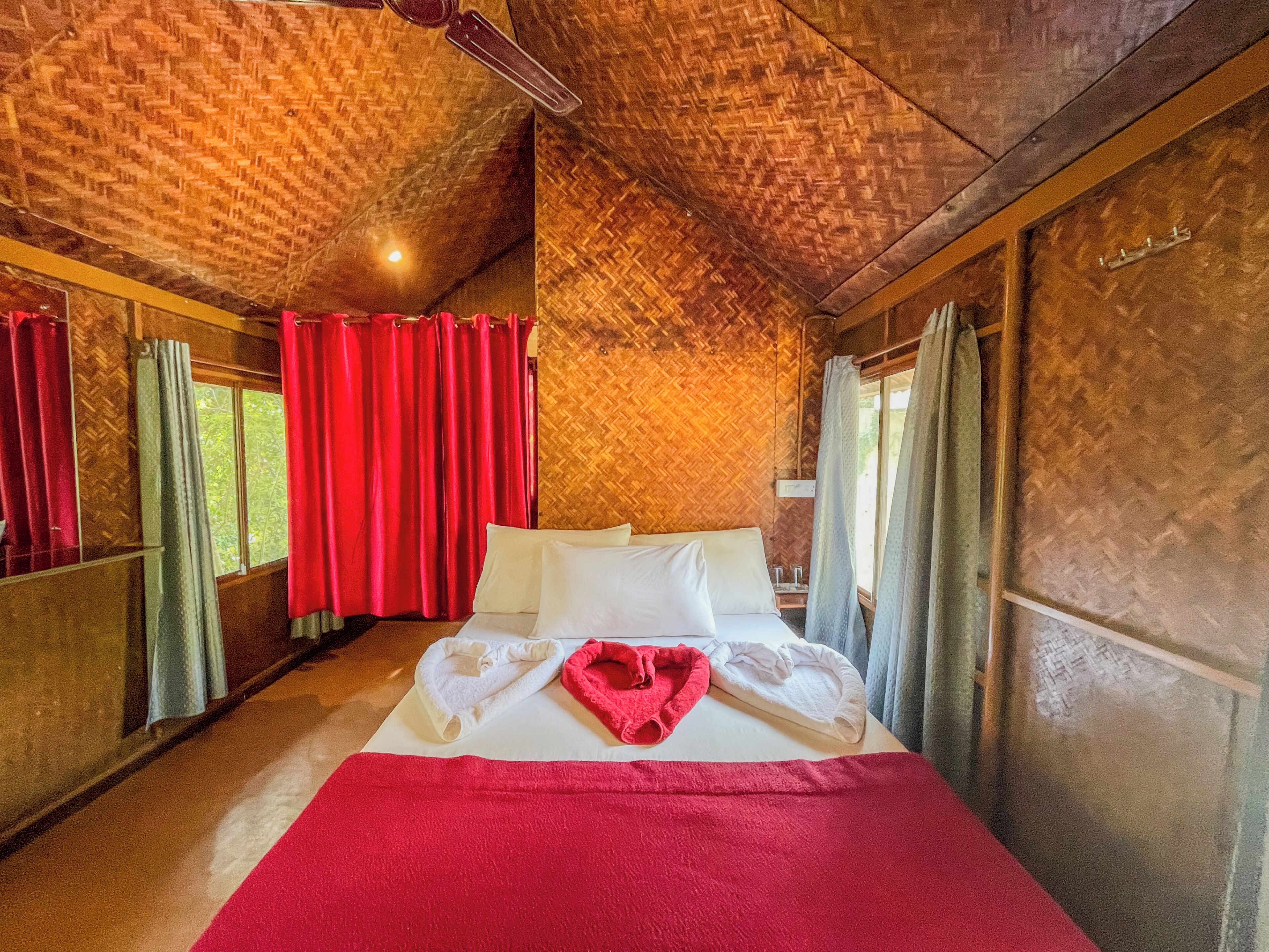 Una habitación con cama, cortinas rojas y techo de madera.
