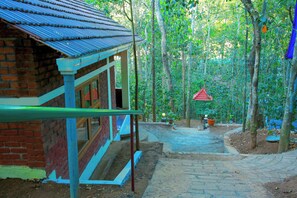 A pathway leading to a building with a blue roof, surrounded by trees. - Snow Hills Nature Resort (Peermade)