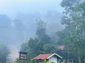 A house with a red roof, surrounded by dense greenery and a foggy background. - Snow Hills Nature Resort (Peermade)