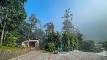 A paved pathway leading to a building with a red roof, surrounded by dense greenery and trees.