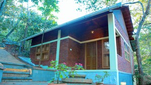 A rustic building with a brick facade, large windows, and a porch area with steps leading up to the entrance. - Snow Hills Nature Resort (Peermade)