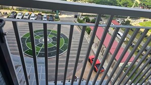 A view from a balcony overlooking a parking area with a circular green space and a red car parked nearby.