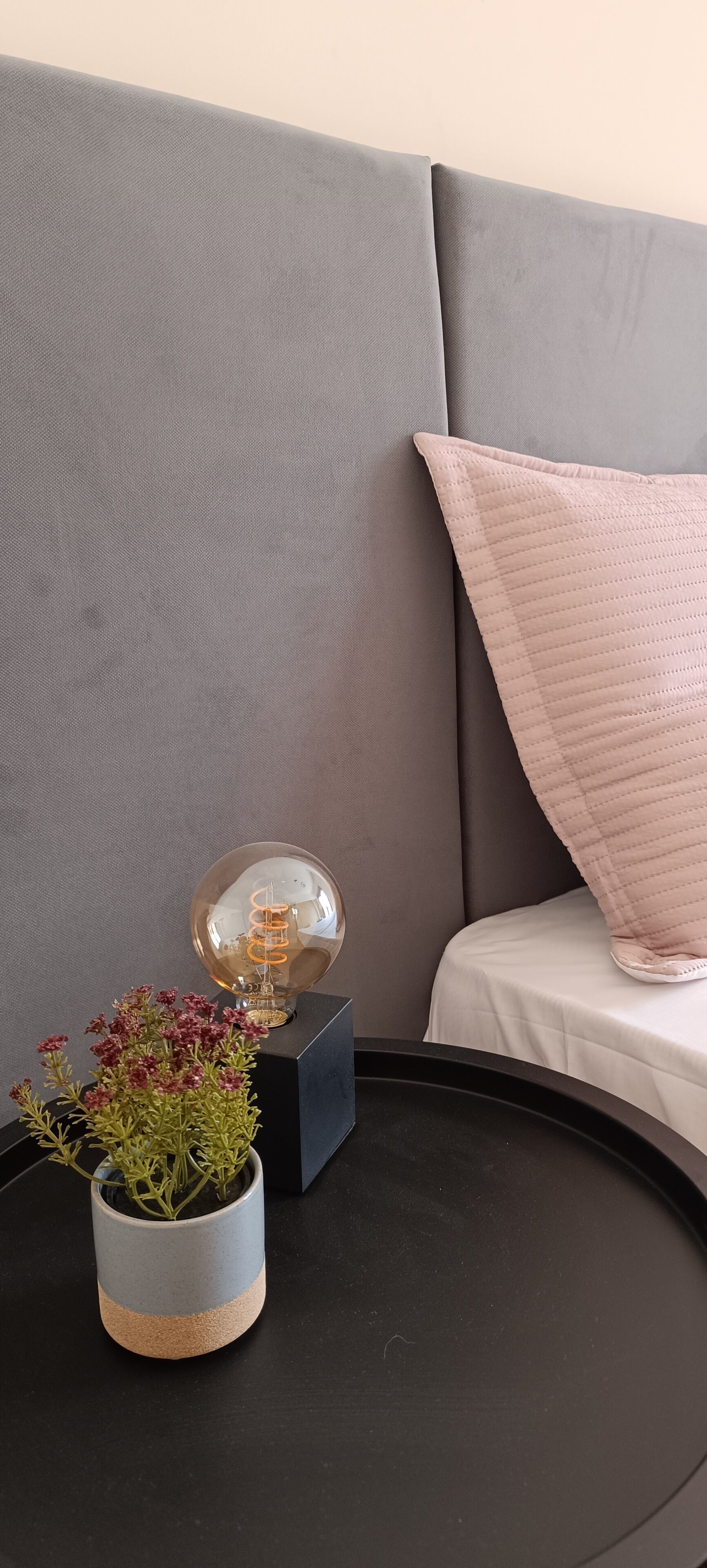 A modern living room with a grey sofa, a round black coffee table, a clear glass sphere with an orange spiral, and a potted plant with red flowers.