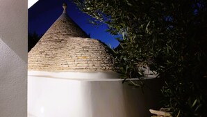 A stone-roofed structure with a white wall and a small window, surrounded by greenery. - Unique Trullo enchantment among olive trees (Noci)
