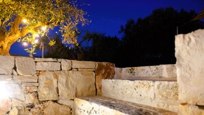 A stone bench with a stone wall and a tree illuminated by street lamps. - Unique Trullo enchantment among olive trees (Noci)
