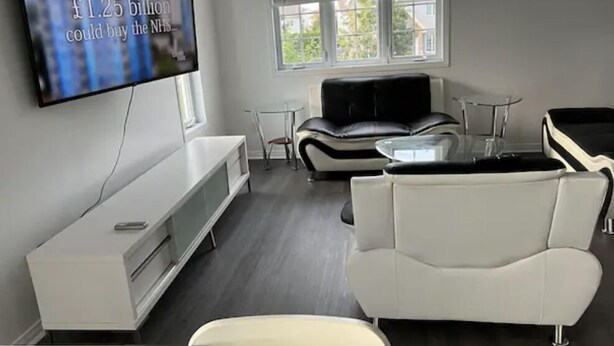 A modern living room with a flat-screen TV, a white sofa, a black leather couch, and a glass coffee table.