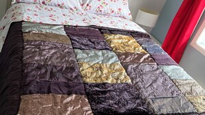 A bed with a white metal frame, a floral-patterned pillow, and a multicolored quilt.