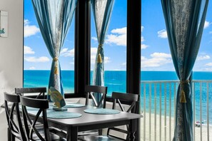 A balcony with a view of the ocean, a table with chairs, and blue curtains tied with tassels.