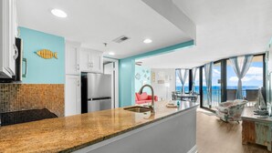 A modern kitchen with a granite countertop, white cabinets, and a view of the ocean through large windows.