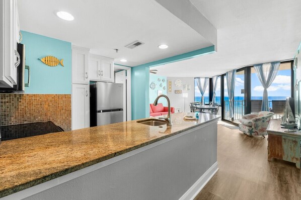 A modern kitchen with a granite countertop, white cabinets, and a view of the ocean through large windows.