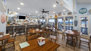 Un restaurante con mesas y sillas de madera, una zona de bar y vistas al océano.
