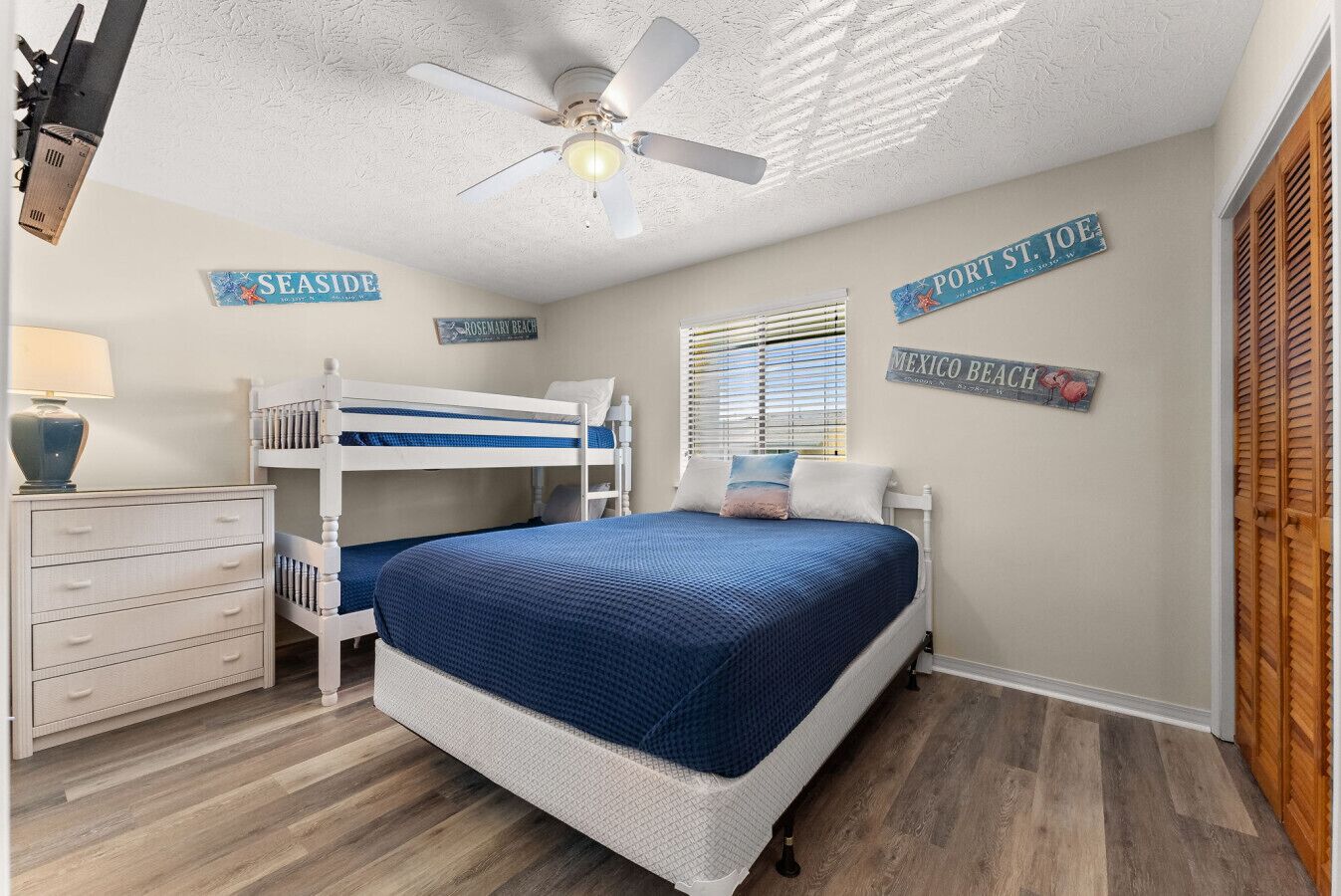 Un dormitorio con literas, ventilador de techo y decoraciones en la pared que dicen "SEASIDE", "ROSEMARY BEACH", "PORT ST JOE" y "MEXICO BEACH".