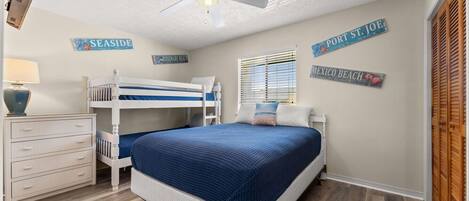 Un dormitorio con literas, ventilador de techo y decoraciones en la pared que dicen "SEASIDE", "ROSEMARY BEACH", "PORT ST JOE" y "MEXICO BEACH".
