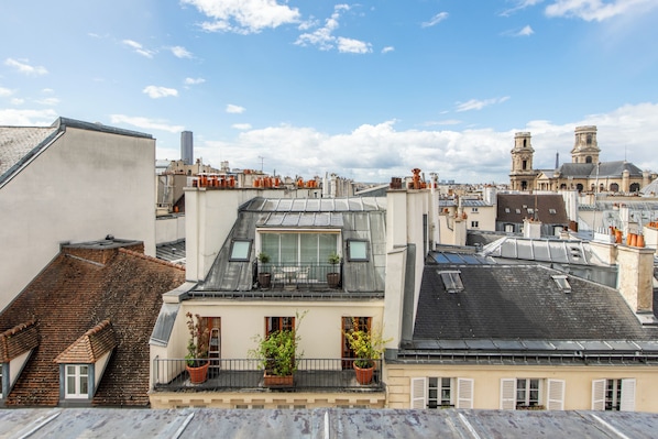 Une terrasse sur le toit agrémentée de plantes en pot, un balcon et une vue sur le paysage urbain.