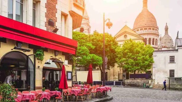Calle empedrada con mesas al aire libre y un edificio histórico con cúpula al fondo.