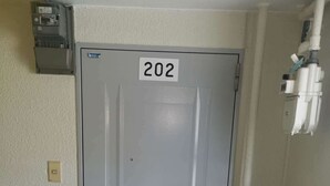A door labeled 202 in a hallway with a light switch and a small electrical box on the wall. - Shin Awaji Building II 202  (Osaka)