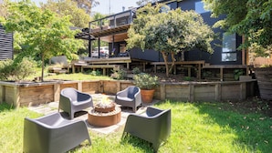 Eine moderne Außenpatio mit eingelassener Sitzgruppe, einem Feuerkorb und einem Holzdeck mit Blick auf einen Garten.