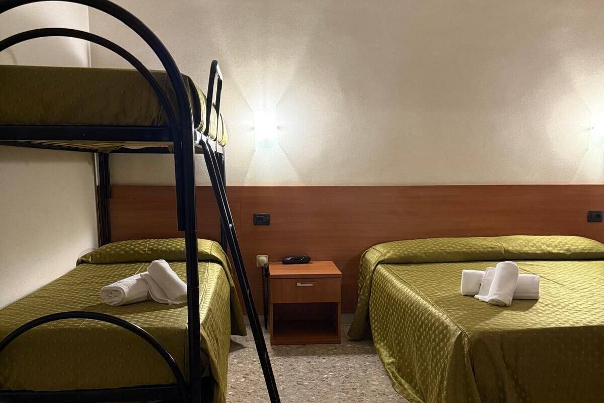 Une chambre avec un lit superposé, deux lits, une table de chevet et une lampe fixée au mur.