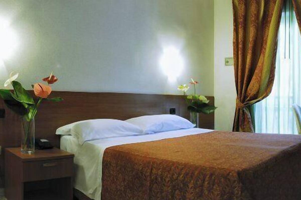 Une chambre d’hôtel comprenant un lit, une table de chevet, une table avec une chaise et une fenêtre avec des rideaux.