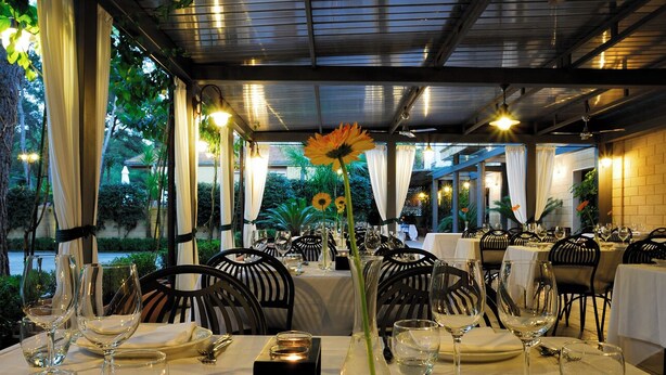Un restaurant où les tables sont dressées pour le dîner, offrant une vue sur la verdure et un coucher de soleil.