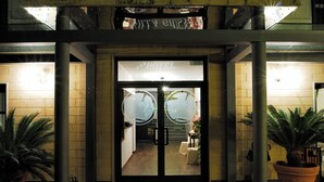 L’entrée d’un hôtel, avec une porte en verre, une enseigne au-dessus de la porte et des plantes en pot de chaque côté.