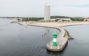 Escena costera con un faro, una playa y un edificio alto al fondo.