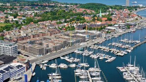 En lysthavn med mange både i havnen, omgivet af en by med bygninger og grønne områder.