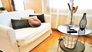 A living room with a white sofa, a round coffee table with a wireframe base, and a small vase with dried branches. - Tiny Shell House (Piran)
