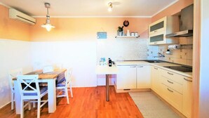A compact kitchen with white cabinets, a wooden dining table, and a small countertop. - Tiny Shell House (Piran)