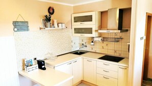 A compact kitchen with white cabinets, a black stove, and a tiled backsplash. - Tiny Shell House (Piran)