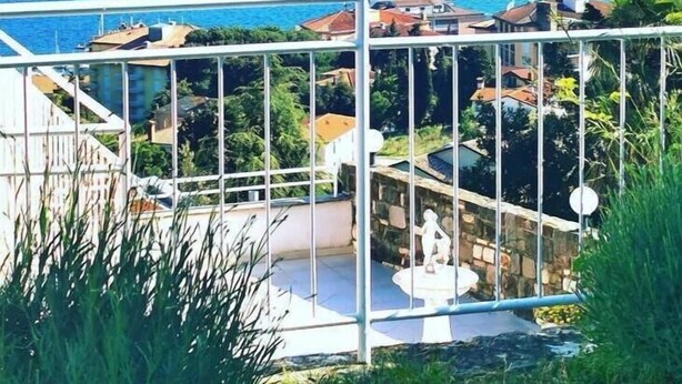 A balcony with a view of a coastal town, a statue, and a clear blue sea. - Tiny Shell House (Piran)